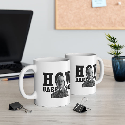 Two white ceramic mugs featuring a stern British soldier with the phrase "How Dare You" in bold text, displayed on an office desk.